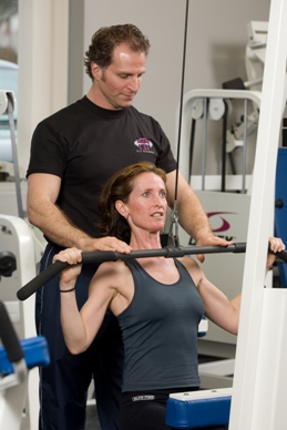 PTP Certified Personal Trainer assisting client with a lat pull down exercise