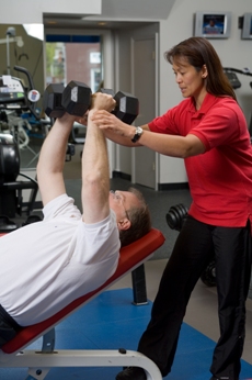 PTP Certified Personal Trainer helping a client do a dumbbell press exercise