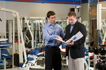 A photo of a PTP trainer showing a new client information on training regimens and gym equipment