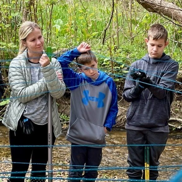 A woman on the left and her two sons on the right are wrapped in blue yarn connecting them to other volunteers on Earth Day