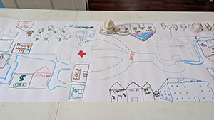 Wide hand-drawn community map showing roads, buildings, a river, and clay sculptures