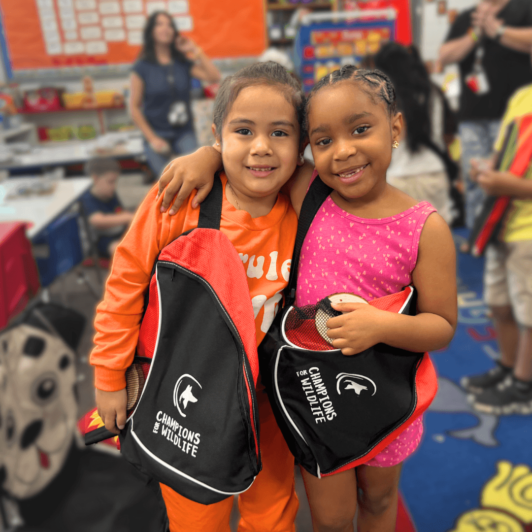 Two first-grade girls side hugging while holding Sunshine & Smiles Kits