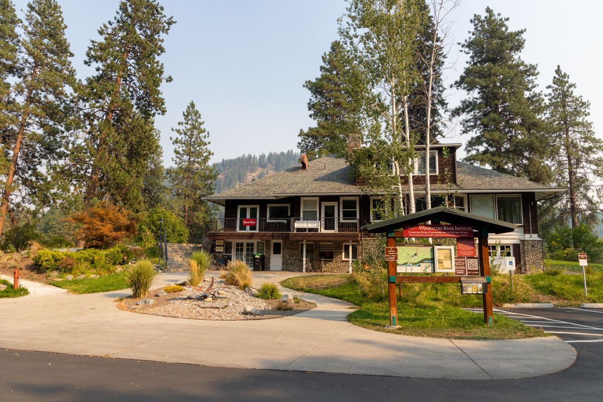 A brown building called the River Haus next to a garden and a pathway, along with a wooden kiosk.