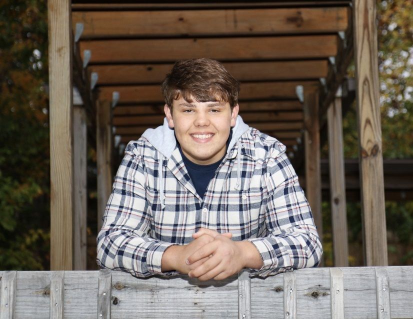 Luke Swearingen leans on a wooden post and smiles.