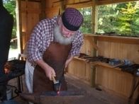 A man blacksmithing in a wooden workshop.