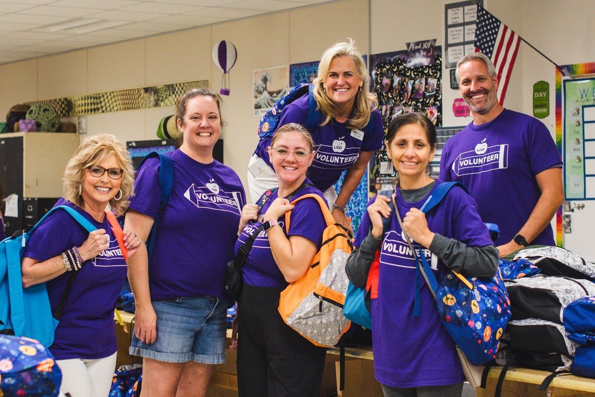 LISD Trustees and LEF Board members pose together and smile holding multiple backpacks filled with school supplies