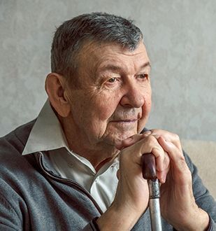 Older man rests his hands on a cane, looking thoughtful