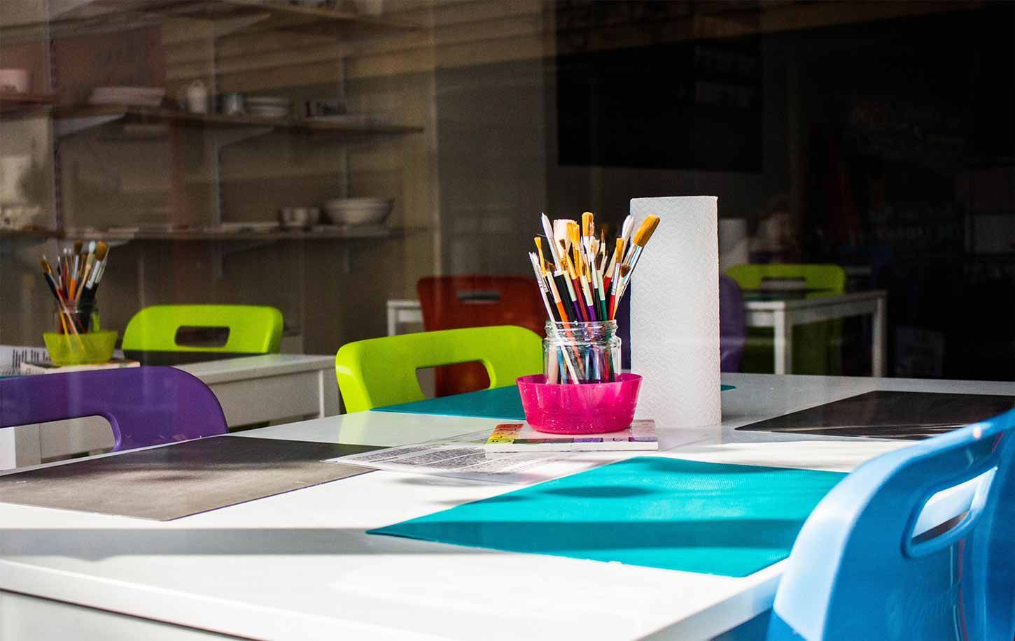 A colorful art room desk with clean paint brushes in a jar.