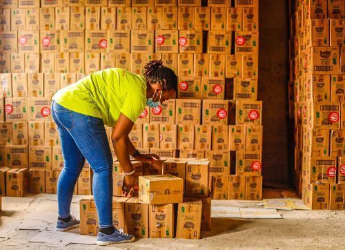 A woman in a t-shirt, jeans, and face mask is bending down to open a cardboard box