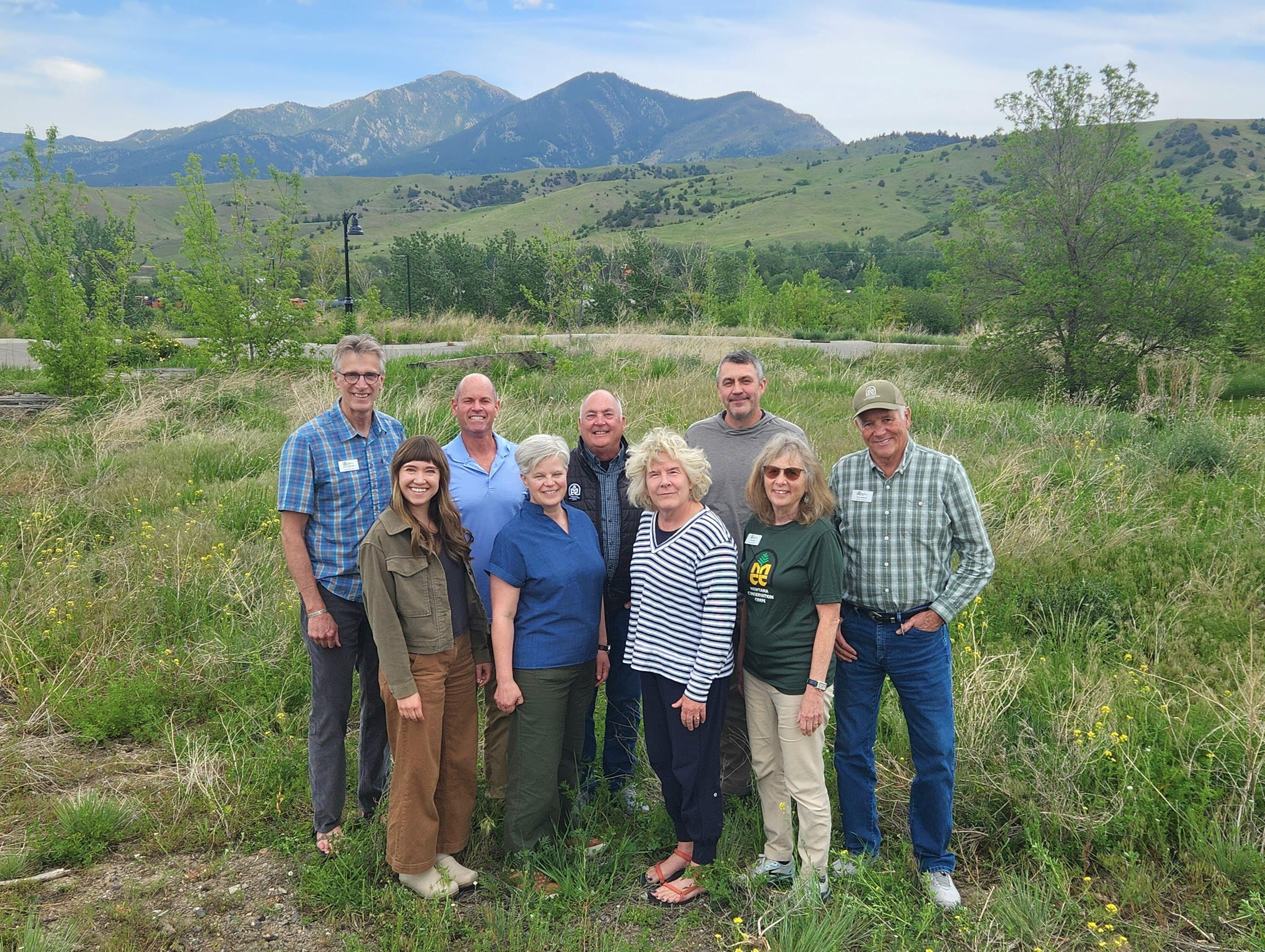[Image Description: Thirteen members of the Board of Directors standing together on an overlook, wearing their MCC jackets and vests. Behind them is a bright blue lake surrounded by trees.]