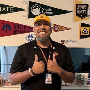 Man giving thumbs up in front of collegiate banners.