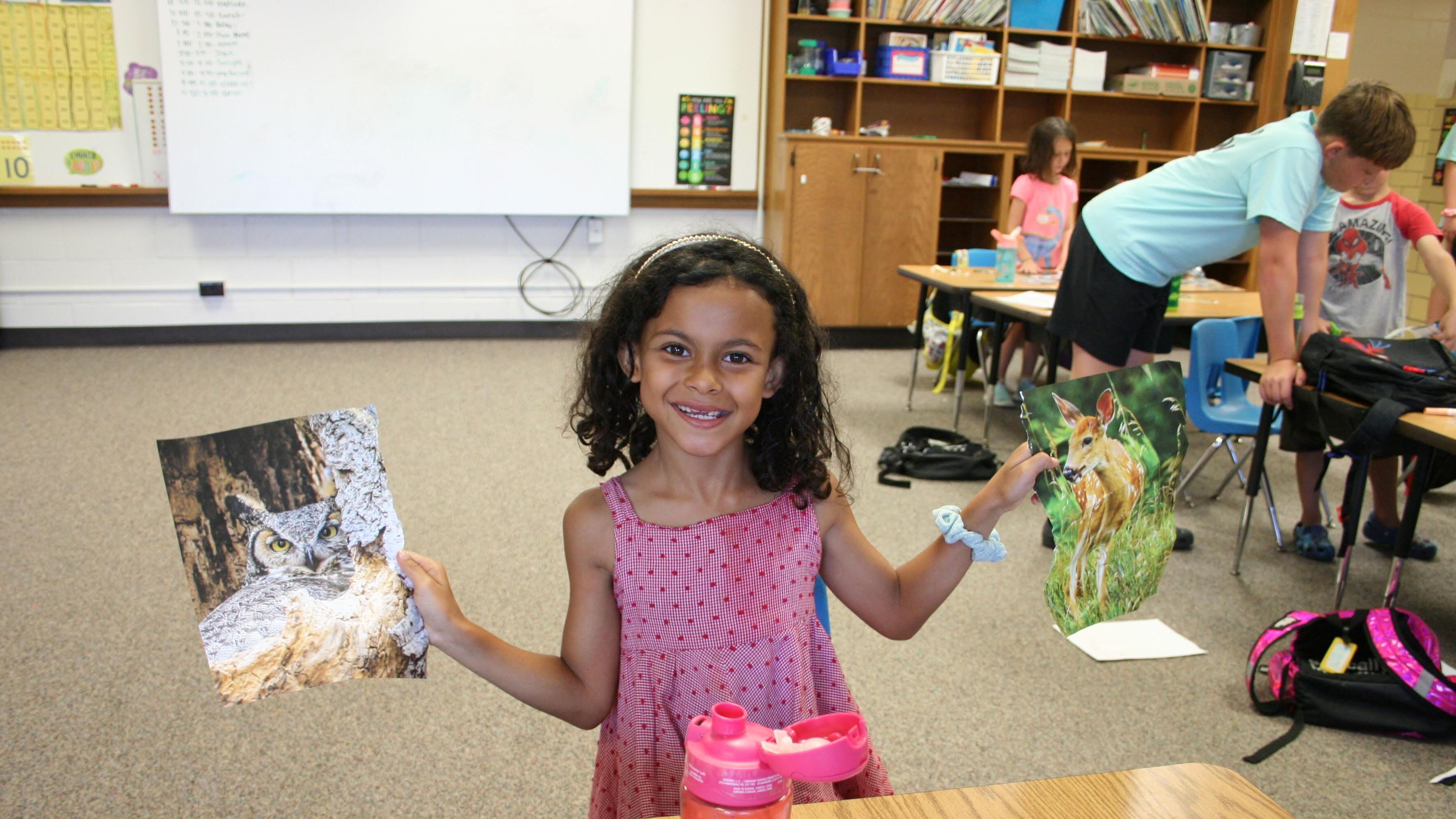 young girl smiling holding pictures of animals in both hands