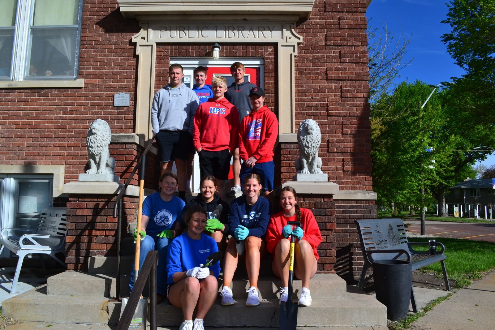 A group of high school students stand on the outside staircase of a brick library