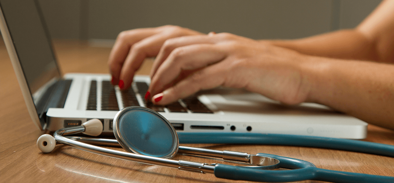 Hands typing at a keyboard with a stethoscope nearby