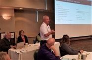 Man speaking to audience at conference with projection screen behind him