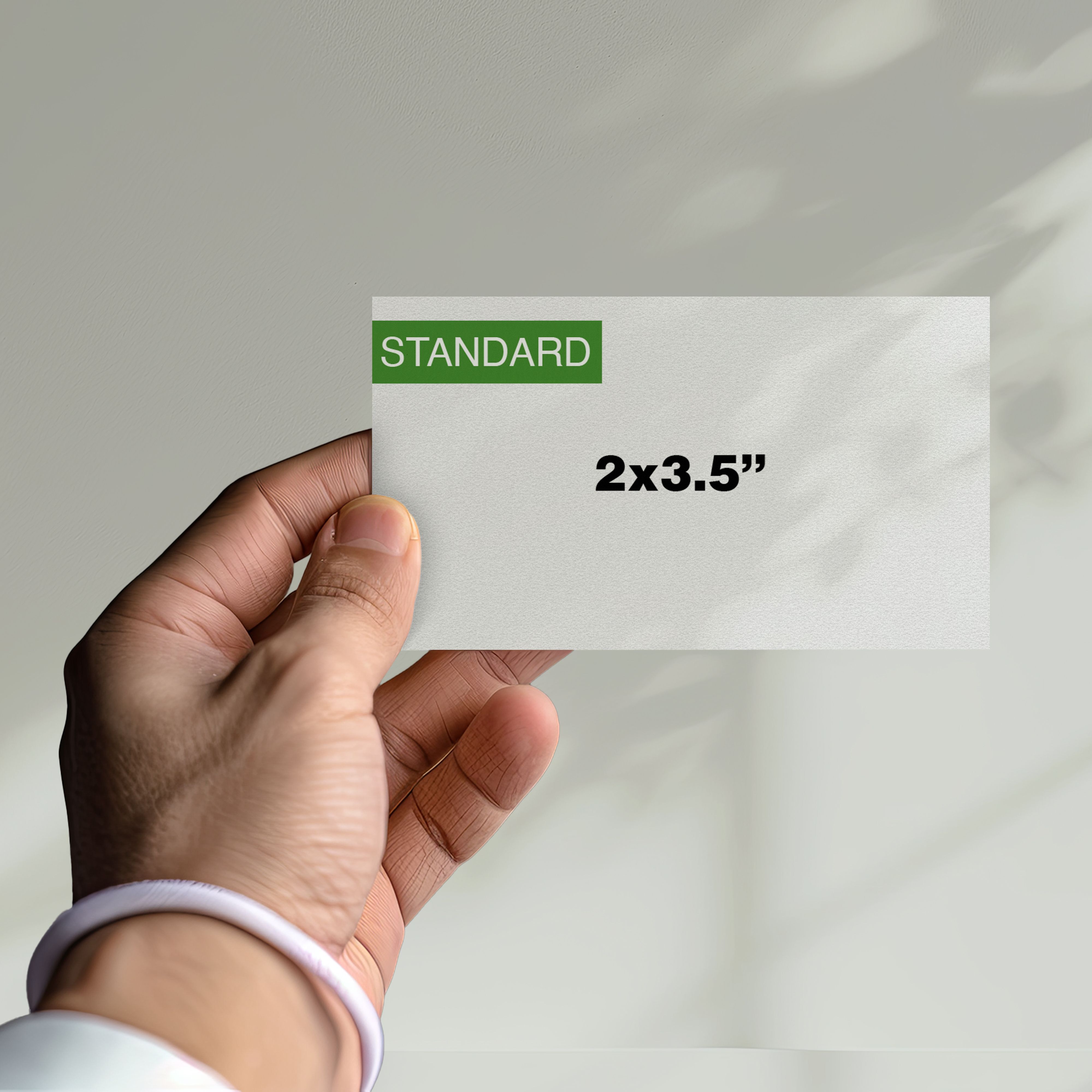 A person holding a white business card labeled “STANDARD” with dimensions 2×3.5 inches printed on it, representing the typical U.S. business card size.