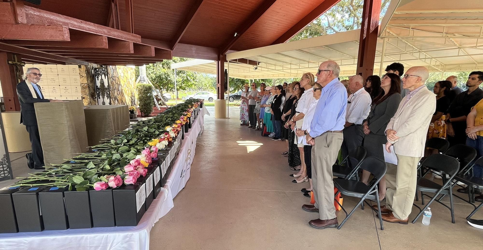 Father Gabriel Ghanoum speaks at the No One Buried Alone service behind the 252 rose-draped containers of cremated remains.