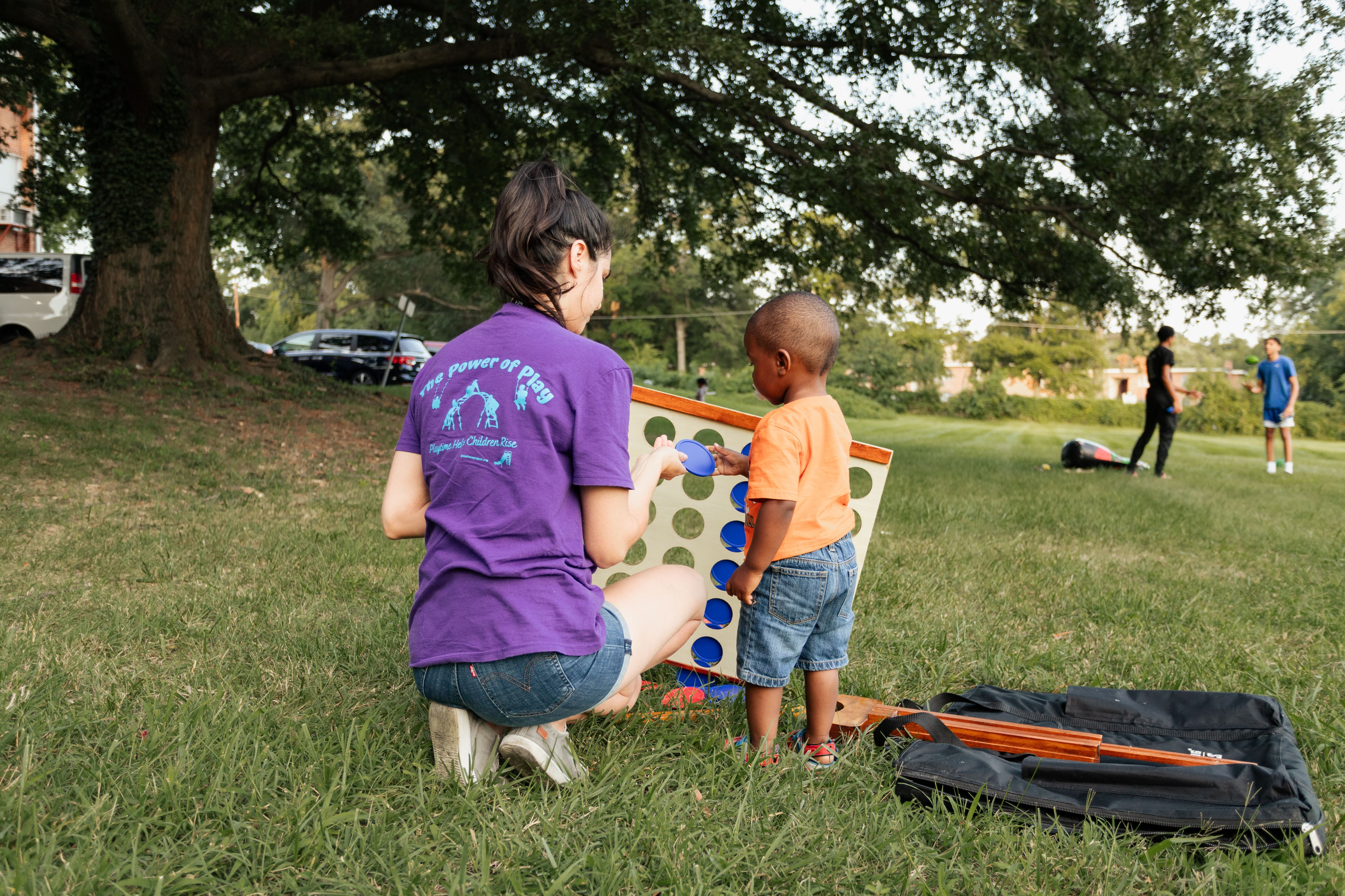Adult woman helping toddler play with a life-sized Connect Four game.