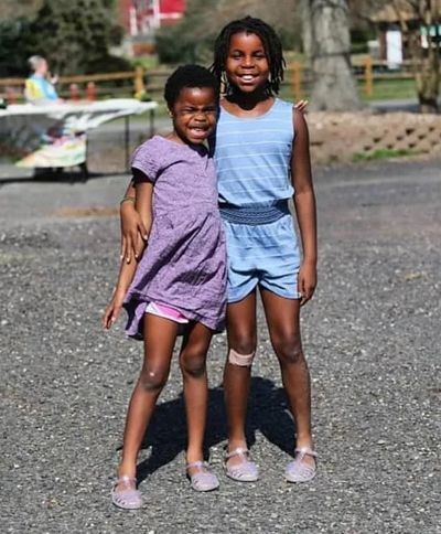 Two African American girls stand shoulder to shoulder hugging each other