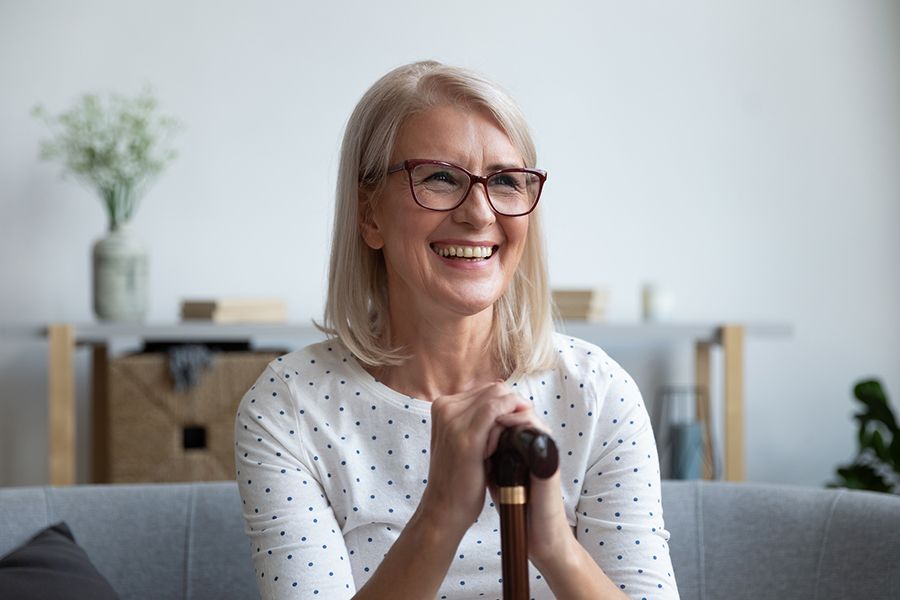 Older woman with a cane smiling and sitting on a sofa