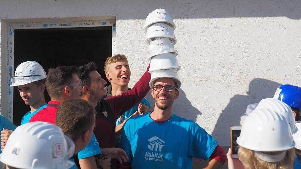 Group of volunteers stacking hard hats on a friend.