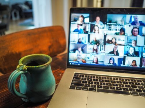 A mug sits on a table next to a laptop displaying a virtual meeting.