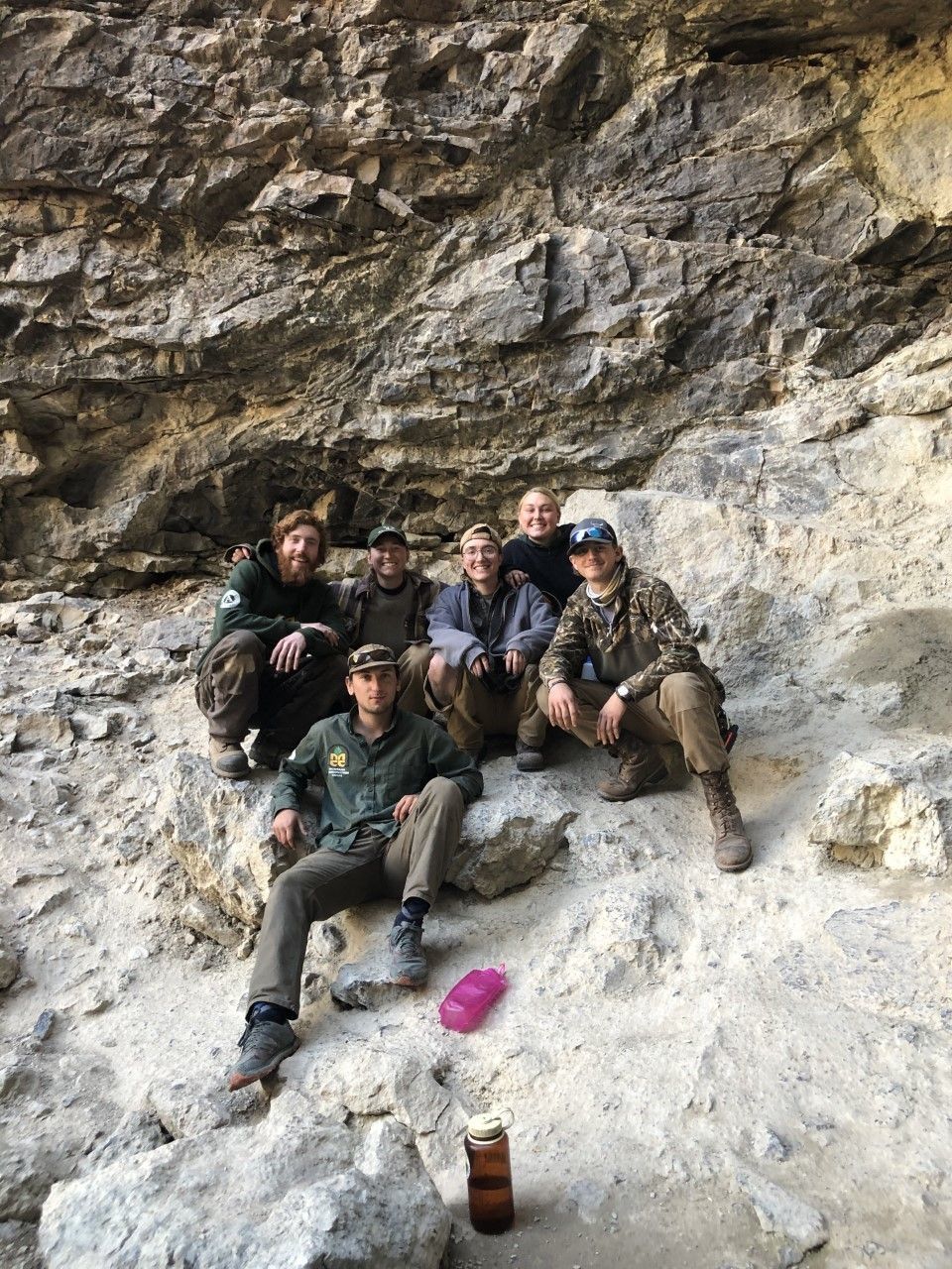 A crew sits together smiling in front of a rock wall