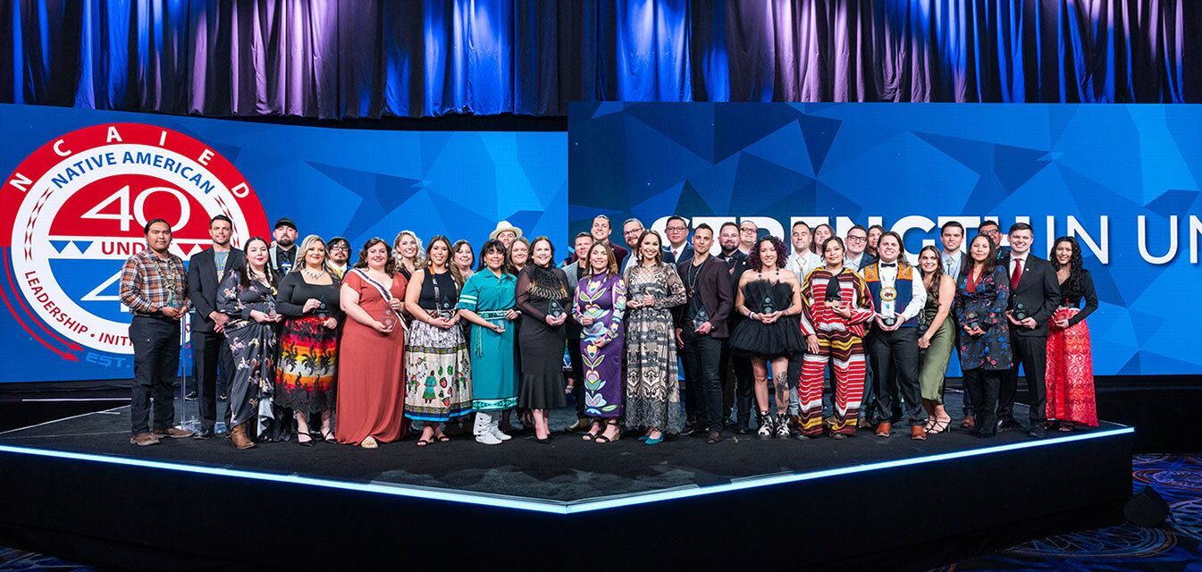 Group of people who are 40 under 40 winners holding their awards on stage.