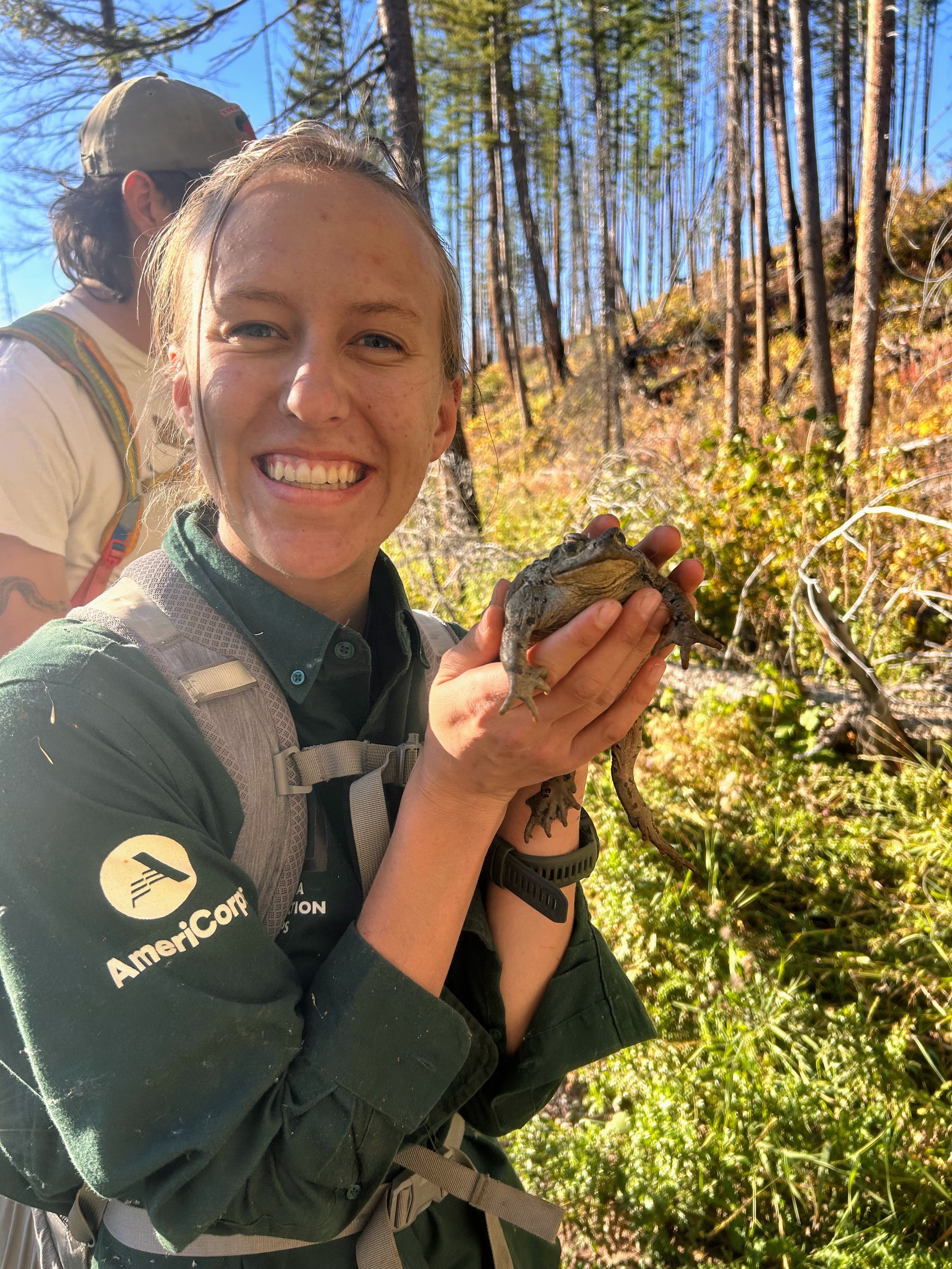 A field crew member holds a large toad and smiles at the camera