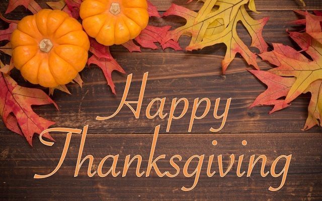 Autumn leaves and pumpkins on a wooden table surrounding the phrase, "Happy Thanksgiving."