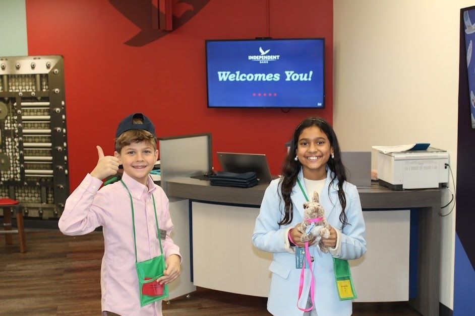 photo of students at Junior Achievement BizTown. Boy giving thumbs up and girl smiling in front of Independence Bank logo on screen