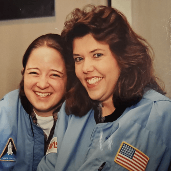 Photograph of Lisa Austgen in a blue NASA space jacket, smiling widely as she experiences a Challenger Learning Center.