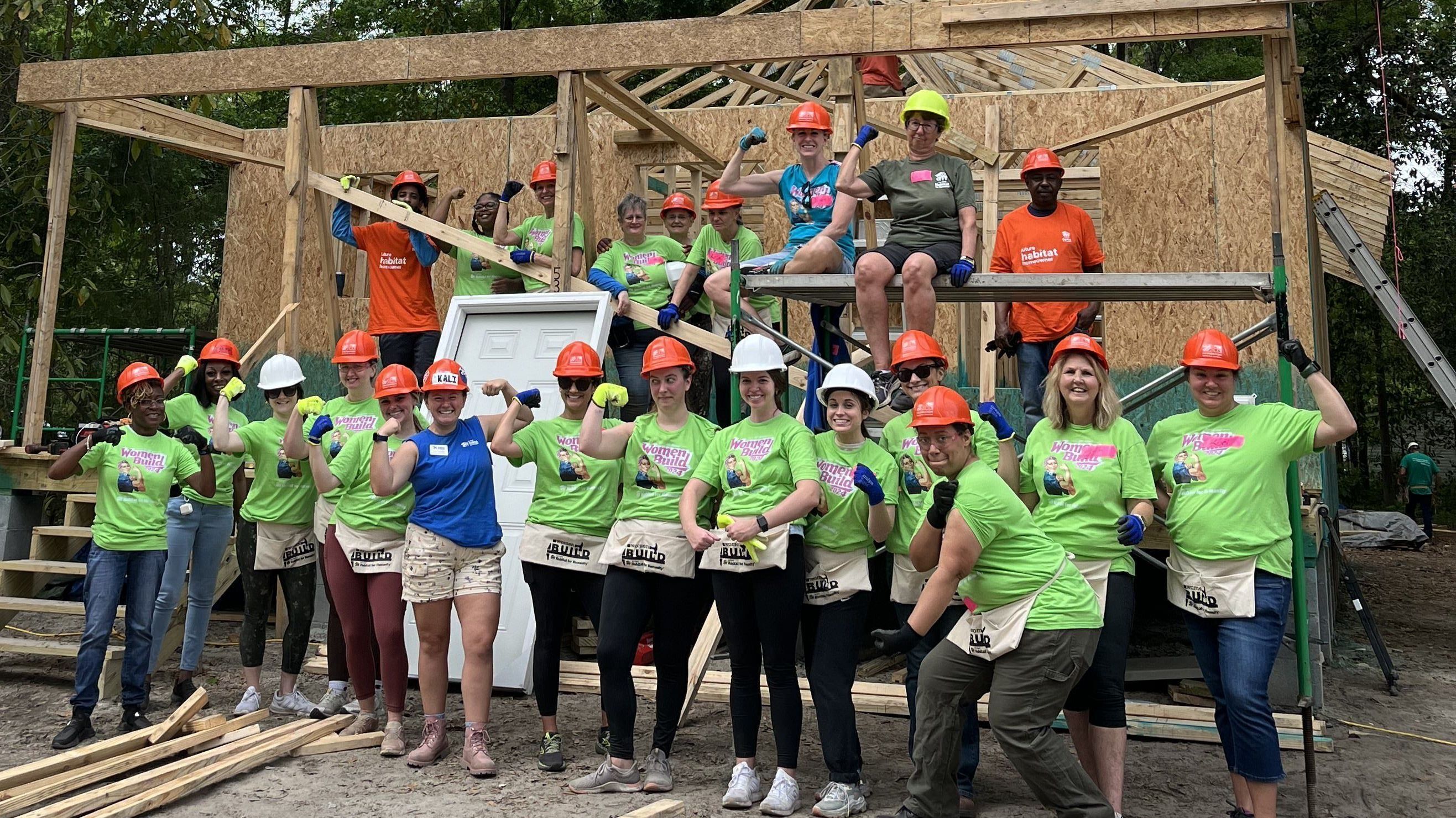 Women on construction site with Women Build shirts on flexing their arm muscles