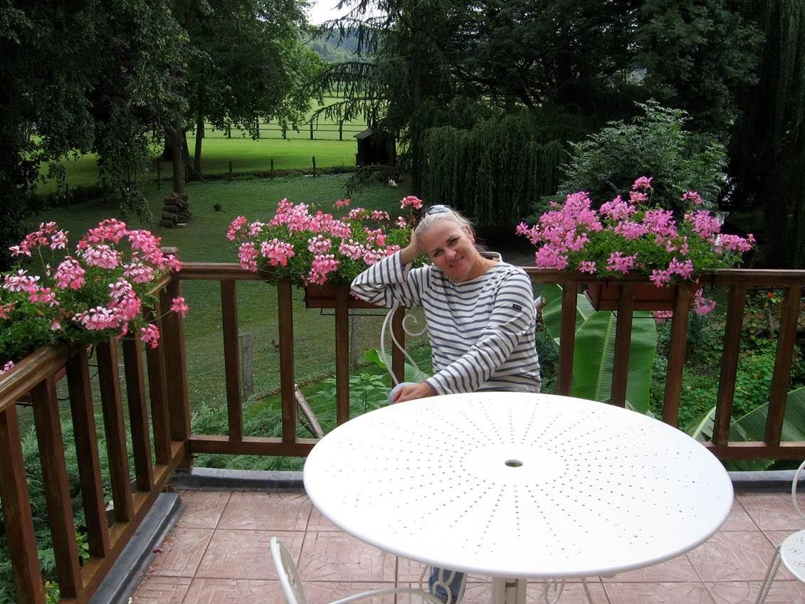 Moira sitting at a circular white table on a wood deck in front of green backyard with pink flowers