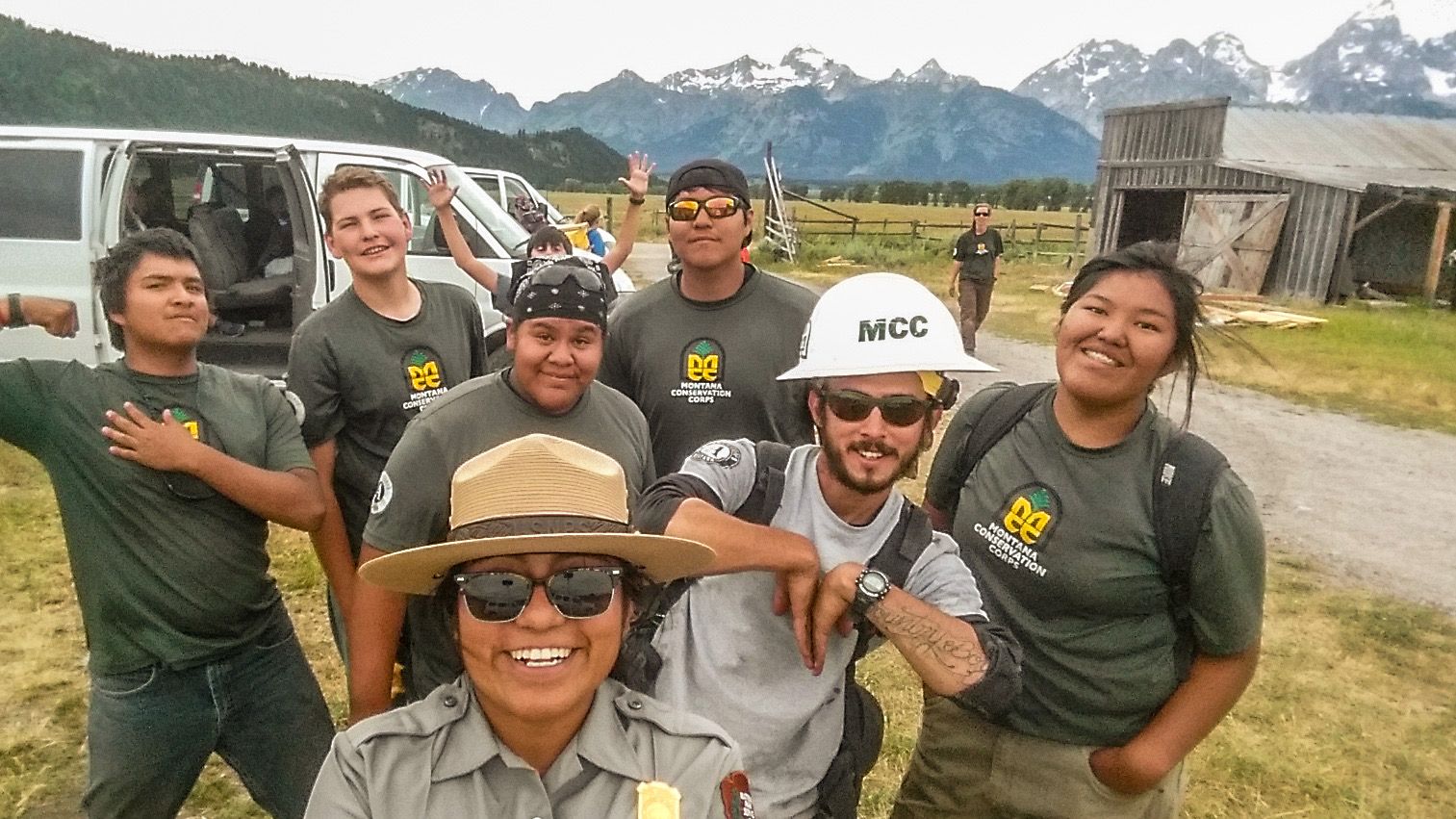 [Image Description: A selfie of eight MCC members and a Grand Teton National Park ranger in front of an old barn with the Teton Mountain Range in the background.]