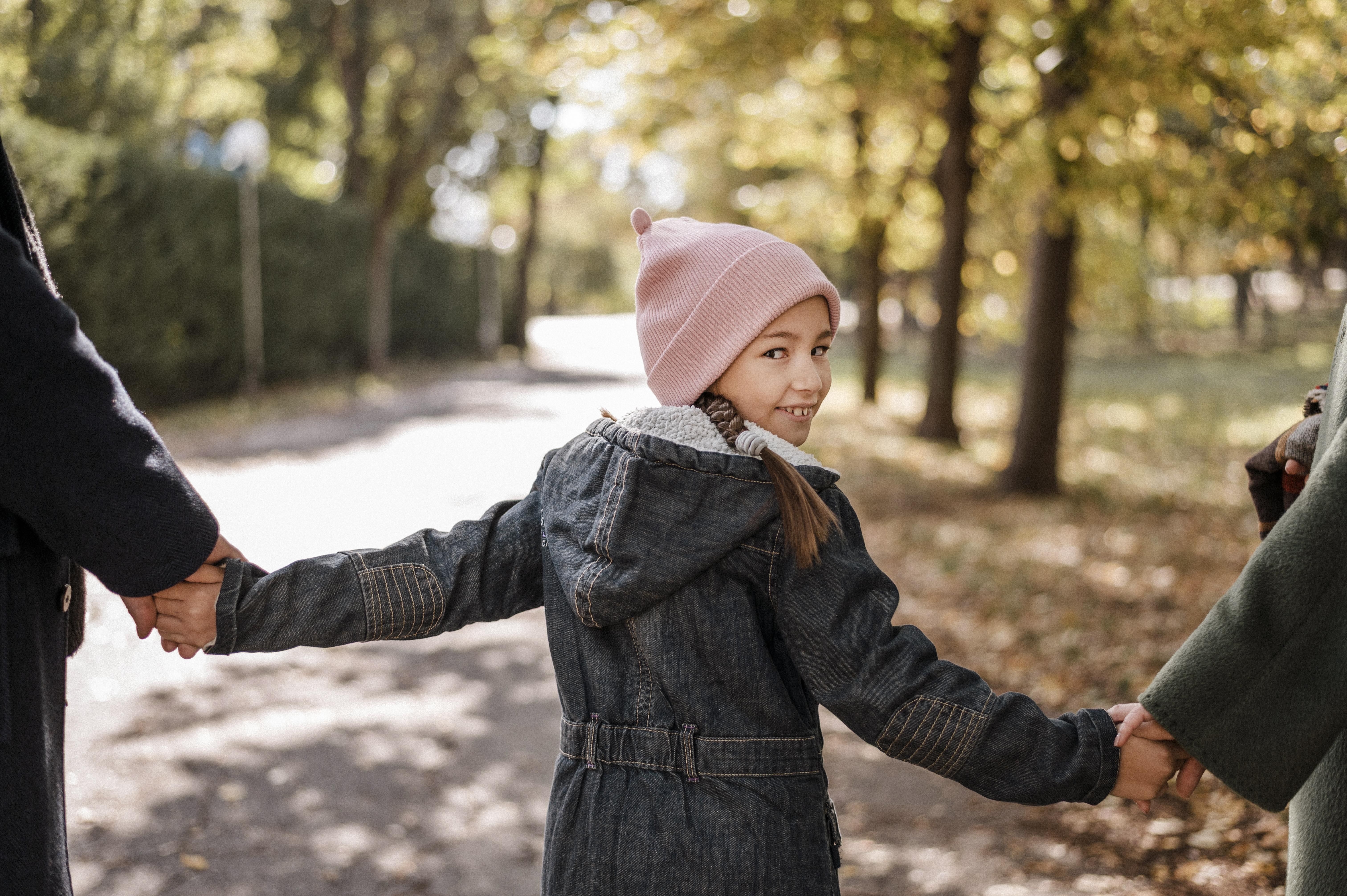 Close-up of a young girl holding hands with both of her parents while walking outside in a park.