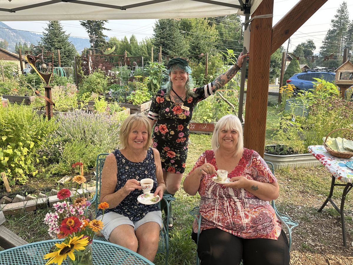 Three people pose for the camera in the garden holding tea.