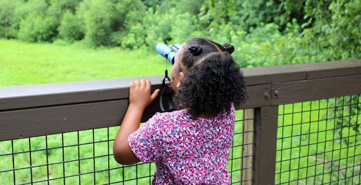 Home for Families Summer Achievers Program student looks through binoculars at Grange Insurance Audubon Center