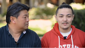 A father and son sit next to each other. The father is looking at his son, who is talking.