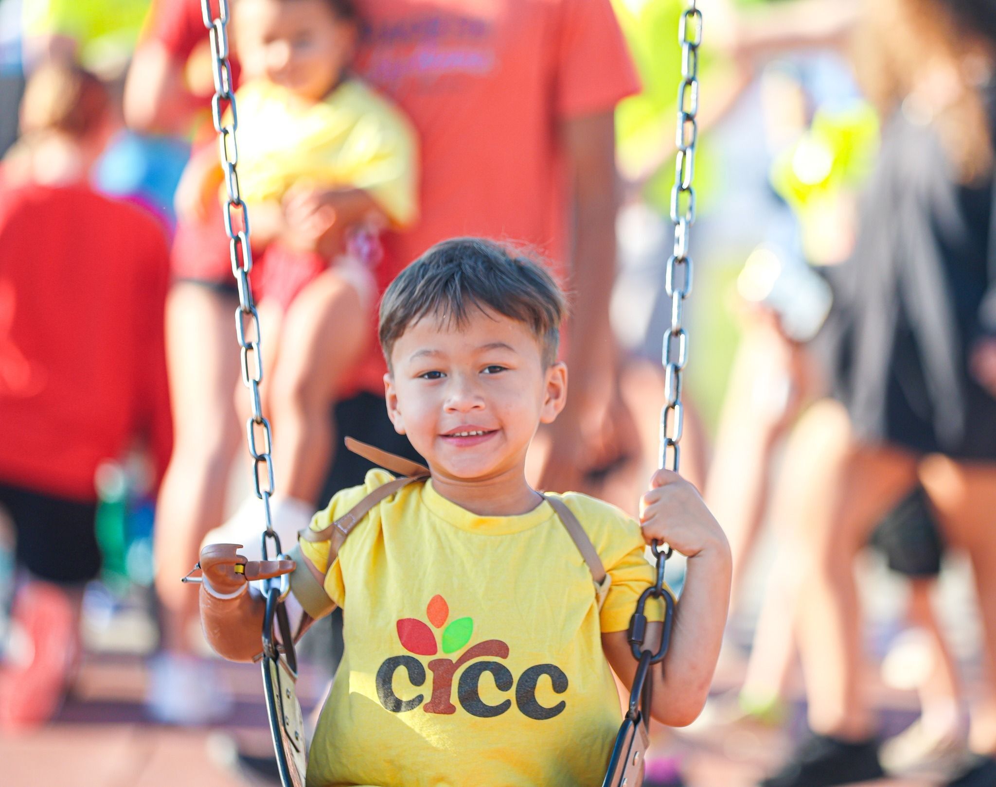 Young boy in CRCC shirt smiling while on the swings at the Race for Big Dreams