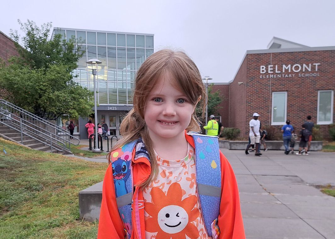 a young girl in an orange jacket posing in front of her school