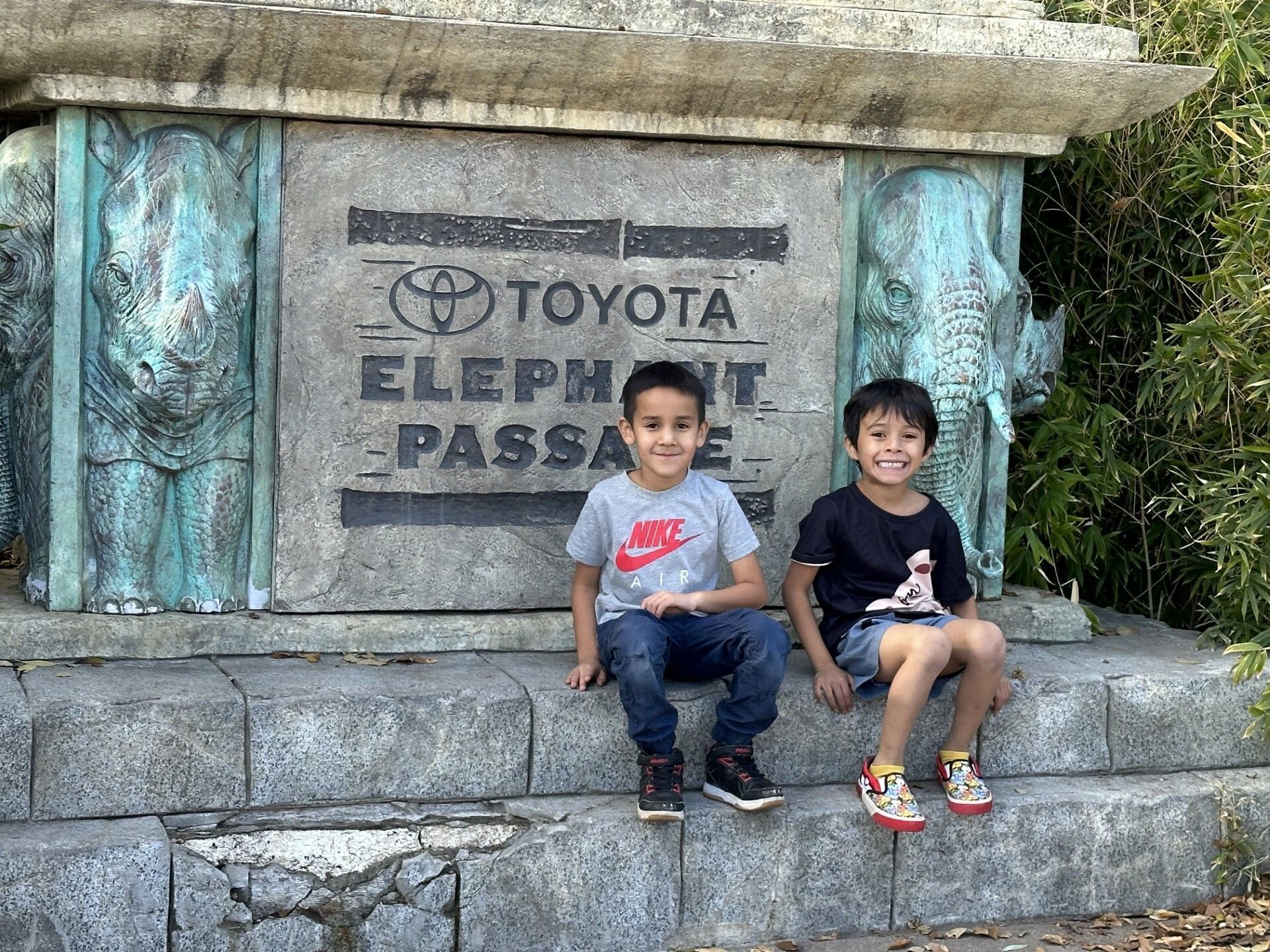 Two young boys smile while sitting in front of the Elephant Passage exhibit at the zoo, representing the joy and learning made possible through field trip experiences.