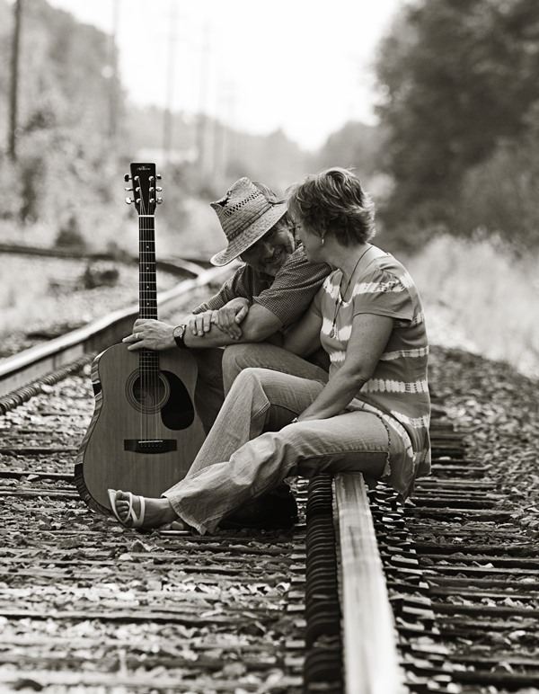 Two people sitting on railroad tracks holding a guitar