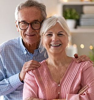 Older couple stand smiling in their home