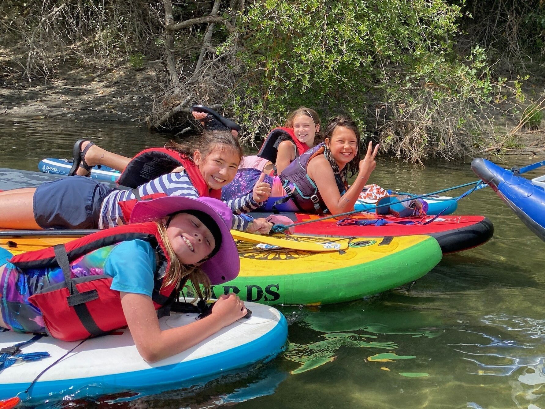 Four campers in PFDs smile for the camera as they lounge on their paddleboards on the Wenatchee River.