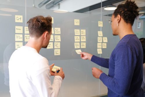 Two people reading notes displayed on a wall.