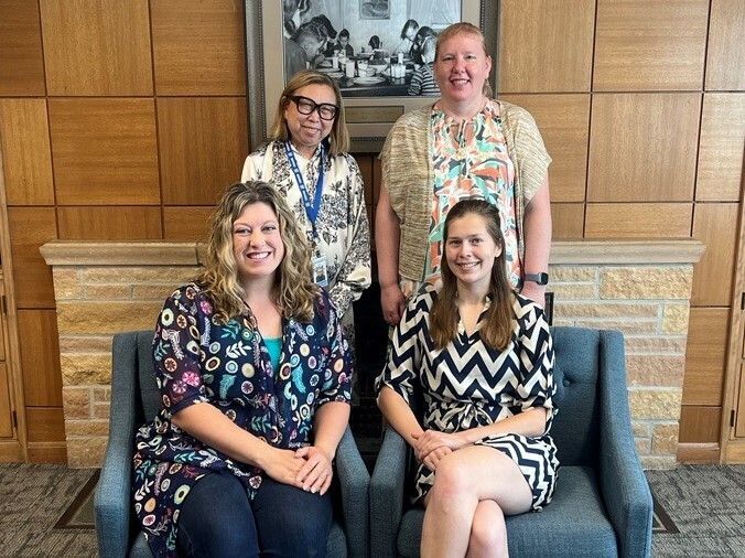 group photo of four women posed. two sitting in chairs in front and two standing behind.