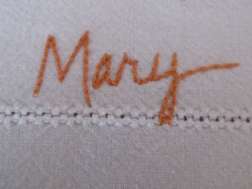 The name Mary embroidered on a table cloth thrifted from Goodwill.