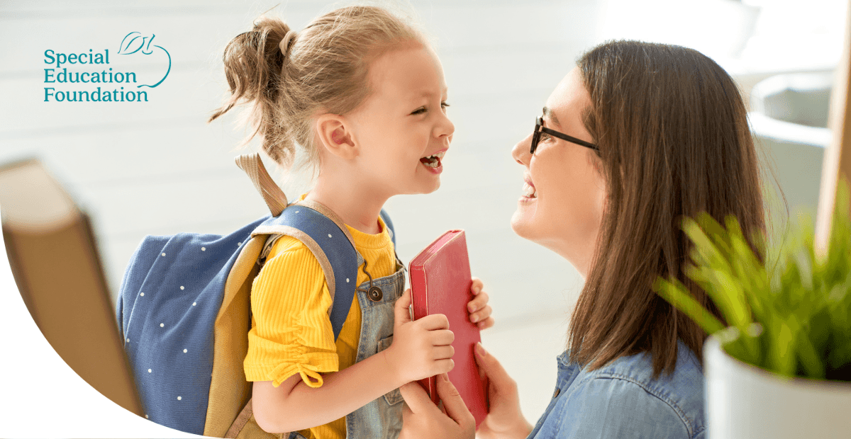 girl smiling and holding a book with a woman in glasses