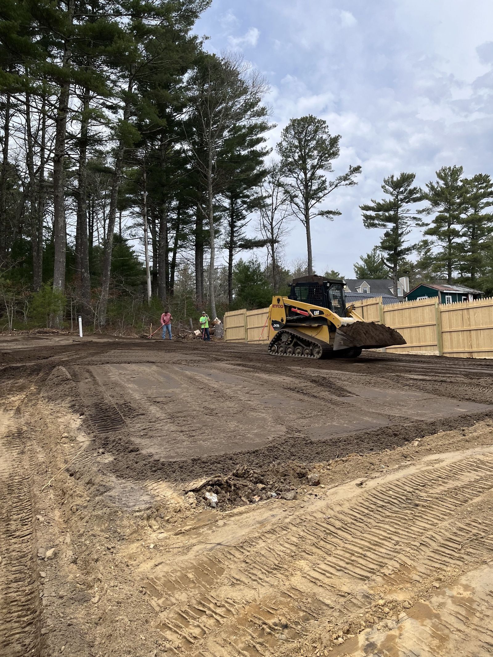 A photo showing a sand and dirt yard with a front loader pouring topsoil